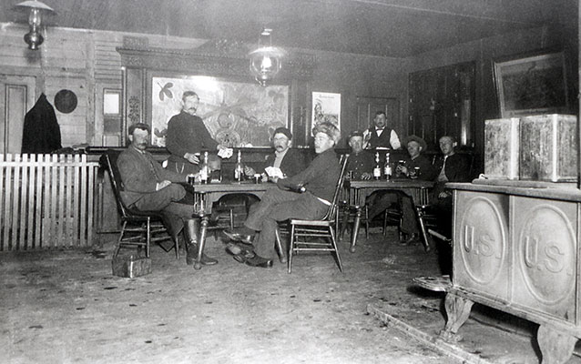 Black-and-white photograph of soldiers sitting around two tables inside the building.