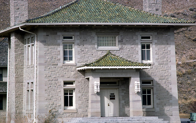 Large, two-story stone building with a green tile roof.