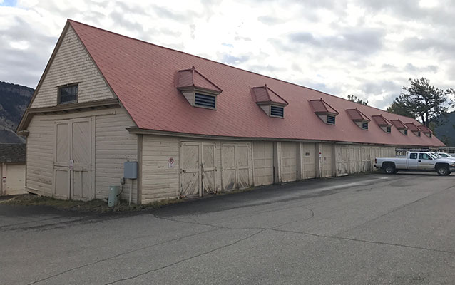 Long, tan wooden building with a red tin roof.