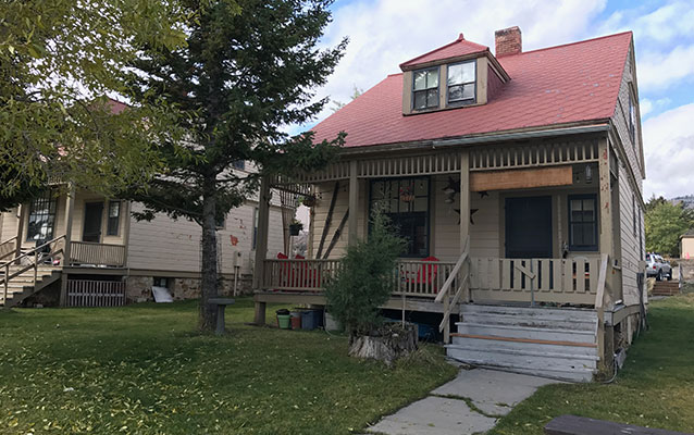 Front of the two-story tan wooden house with a red tin roof.