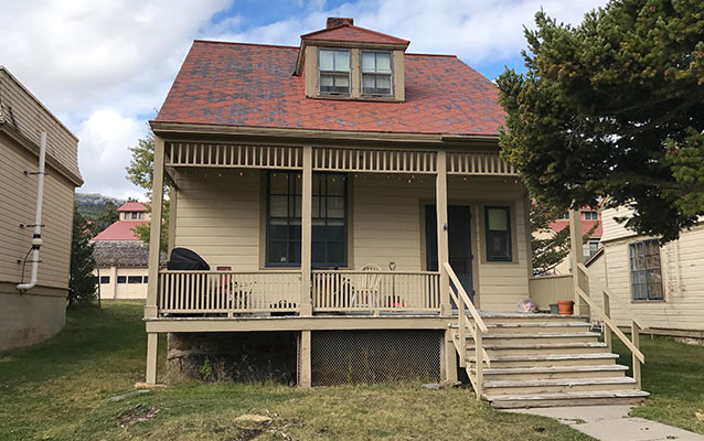 Front of the two-story tan wooden house with a red tin roof.