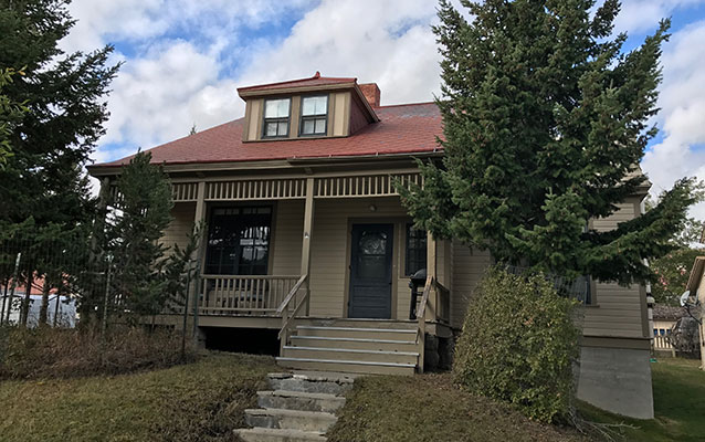 Front of the two-story tan wooden house with a red tin roof.