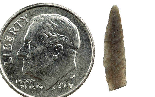 Tiny chipped stone tool next to a dime to show that they are the same length Tiny chipped stone tool next to a dime to show that they are the same length