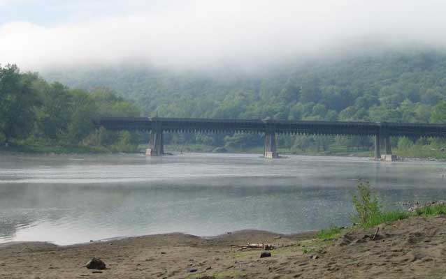 a low bridge over water, seen from shore, green mountains beyond