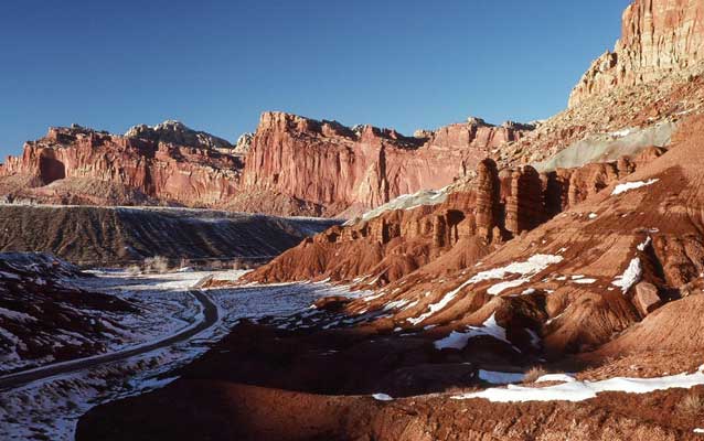 a desert canyon with light snow, dark windy road at bottom of valley a desert canyon with light snow, dark windy road at bottom of valley