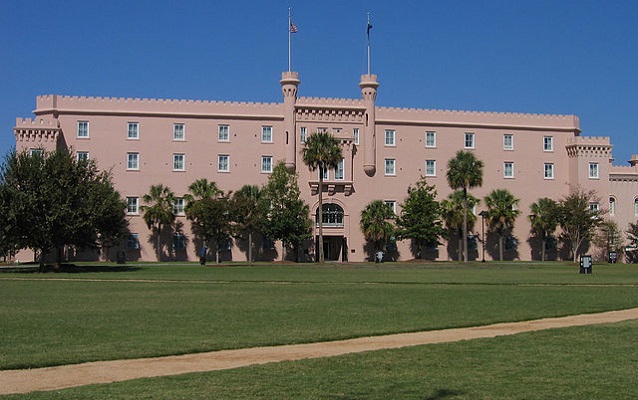 Four-story brick structure in background with green lawn in foreground. 