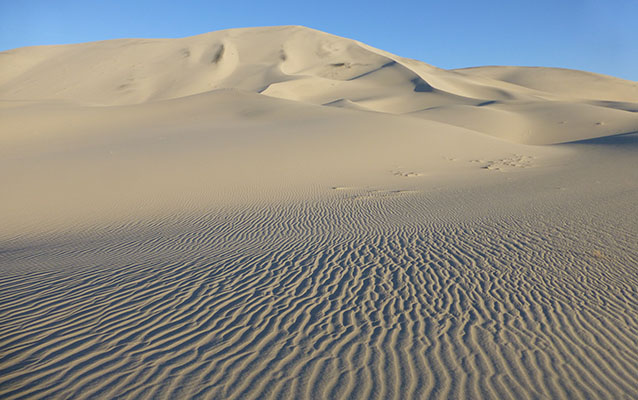Sand ripples in the foreground lead to high dunes in the background. 