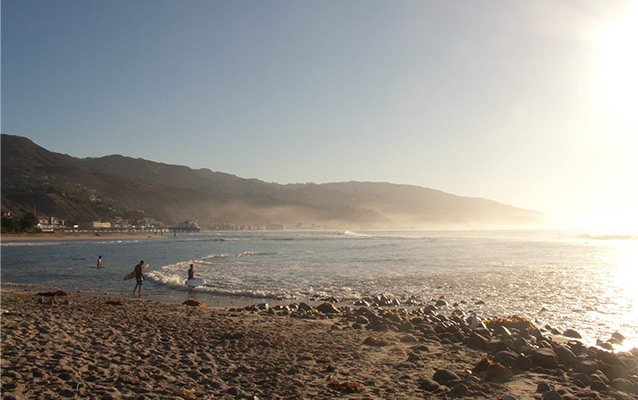 Surfers entering the water at Third Point, with Malibu Pier in the background, camera facing east.