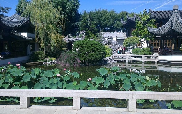 Garden with a pond in foreground and architecture, large rocks, and trees in background. 