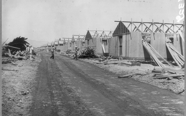 Black and white photo of dirt road running in front of half constructed, one-story buildings. Black and white photo of dirt road running in front of half constructed, one-story buildings.