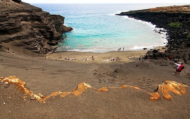 Sandy beach slopping downhill toward the water framed by rock cliffs. 