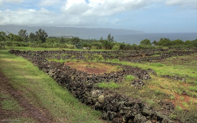 Stone foundations with encroaching grass, trees and sky in background.