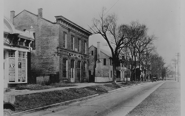 Black and white view along an old road with buildings. Photo by Colonial Williamsburg. Public Domain