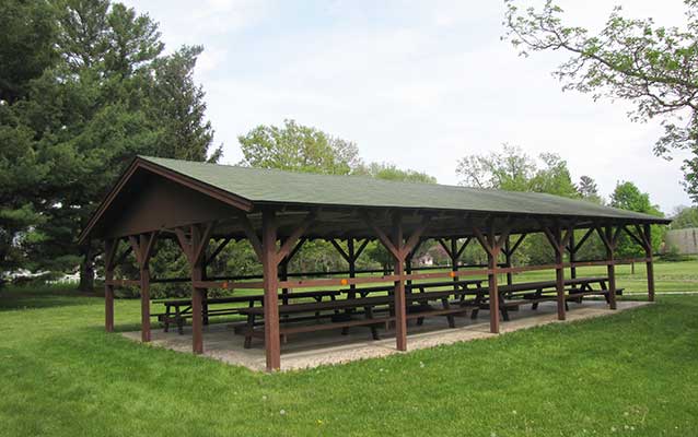 A park picnic shelter has a reddish-brown timber frame and green shingled roof. A park picnic shelter has a reddish-brown timber frame and green shingled roof.