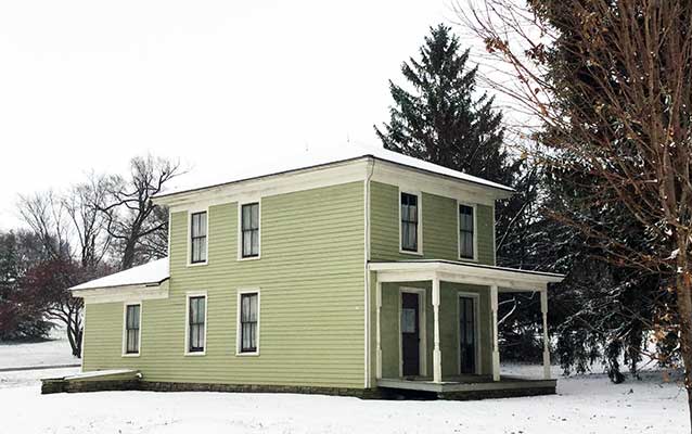 A green two story house has white trim and a porch. A green two story house has white trim and a porch.