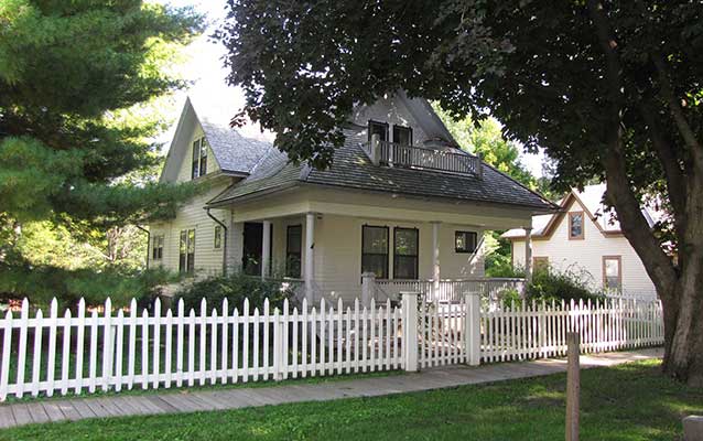 A picket fence encloses a white two-story house with a porch. A picket fence encloses a white two-story house with a porch.