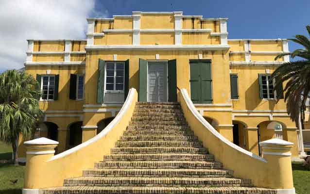 a large yellow building with staircase in front and green shutters