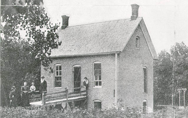 Black and white photo of a house with five people standing in front.