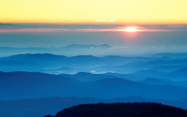 Mountains with a blue tint with a sunset in the background.