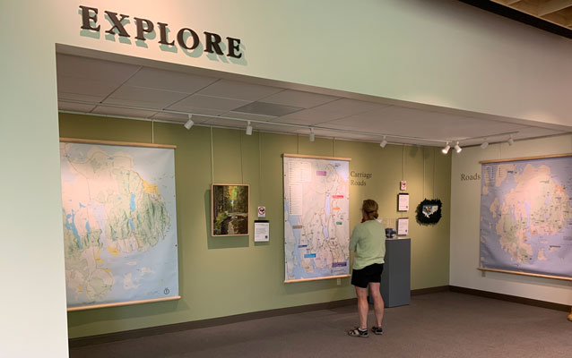 The words 'explore' above an alcove where a visitor looks at hanging maps and art