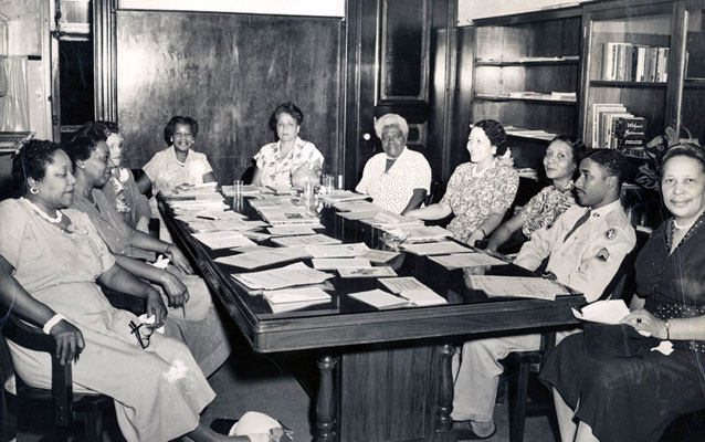 group sits around wooden table in black and white group sits around wooden table in black and white