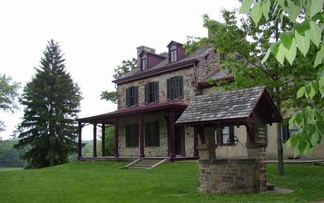 A two story stone house of gray stone, set behind a matching stone well.