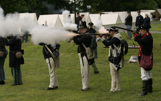 Five soldiers in historical attire fire muskets. Five soldiers in historical attire fire muskets.