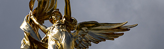 A golden, winged figure holds a flag and holds her arm outstretched.
