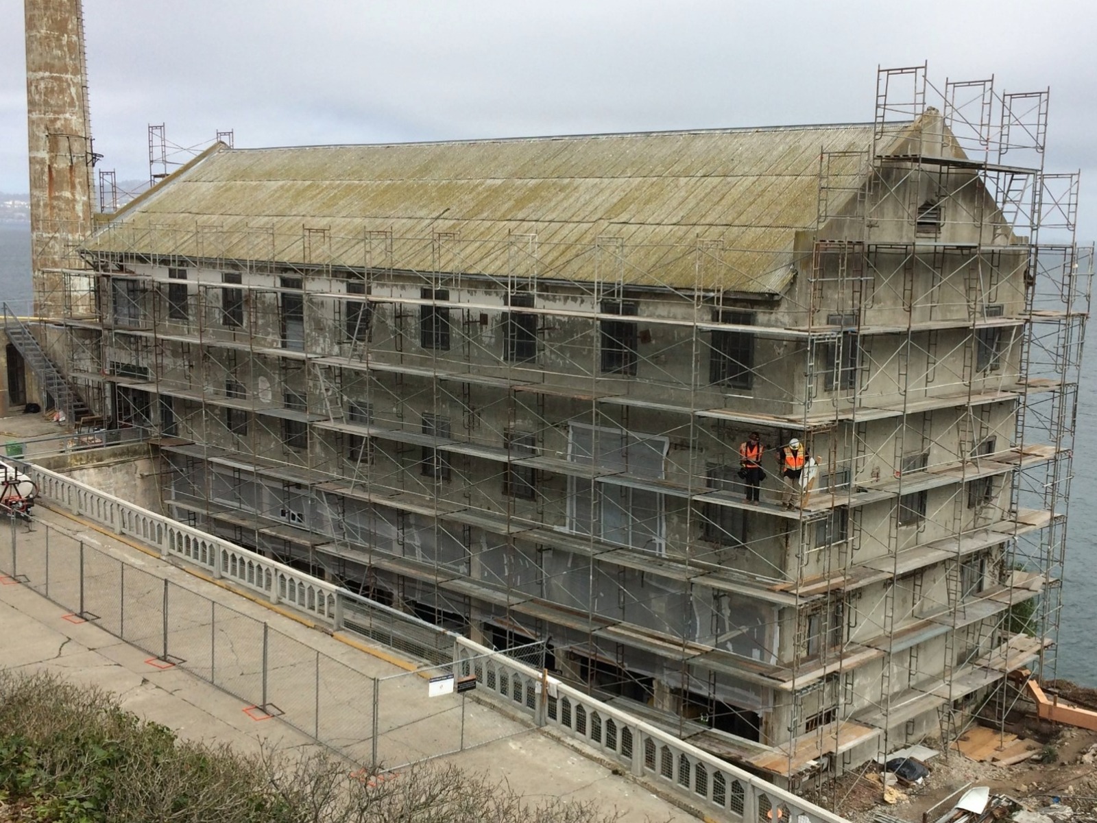 A four story building with scaffolding, flaking paint and moss-covered roof.