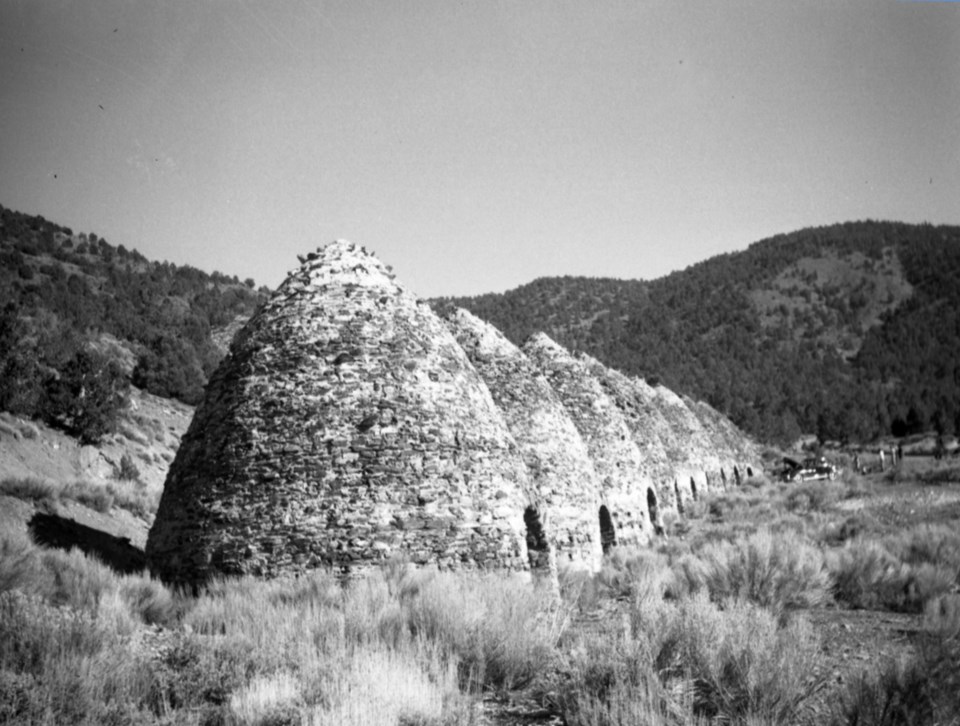 Black & White photo of Conical shaped brick ovens with hills behind