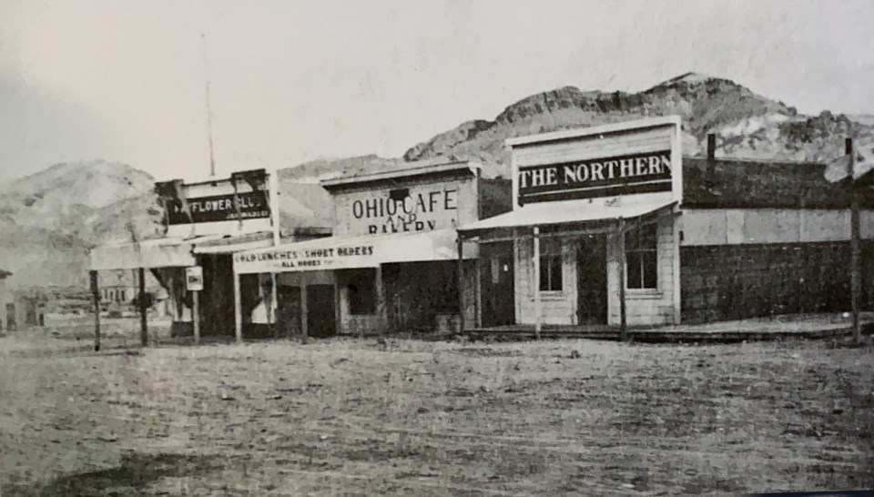 Wooden buildings, dirt street, and mountains in background.