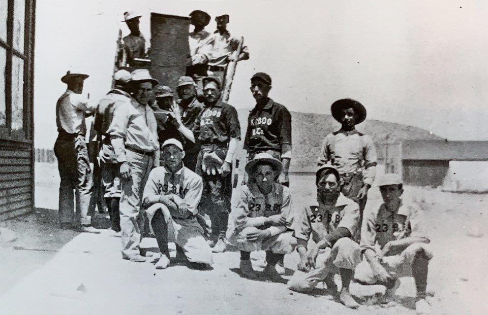 Young men in baseball uniforms next to building.