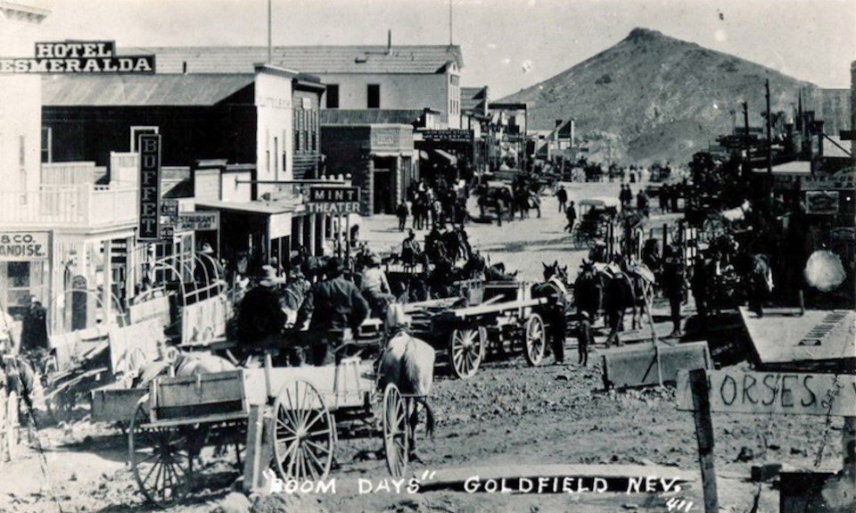 Wagons, people and buildings with mountain in background.