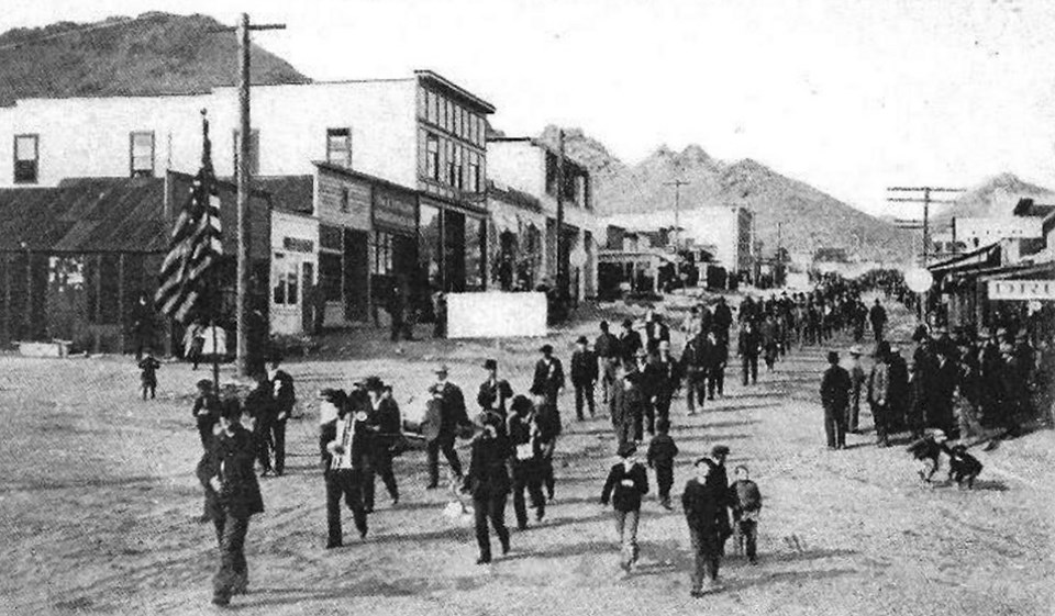 Men marching past buildings with mountains in background.