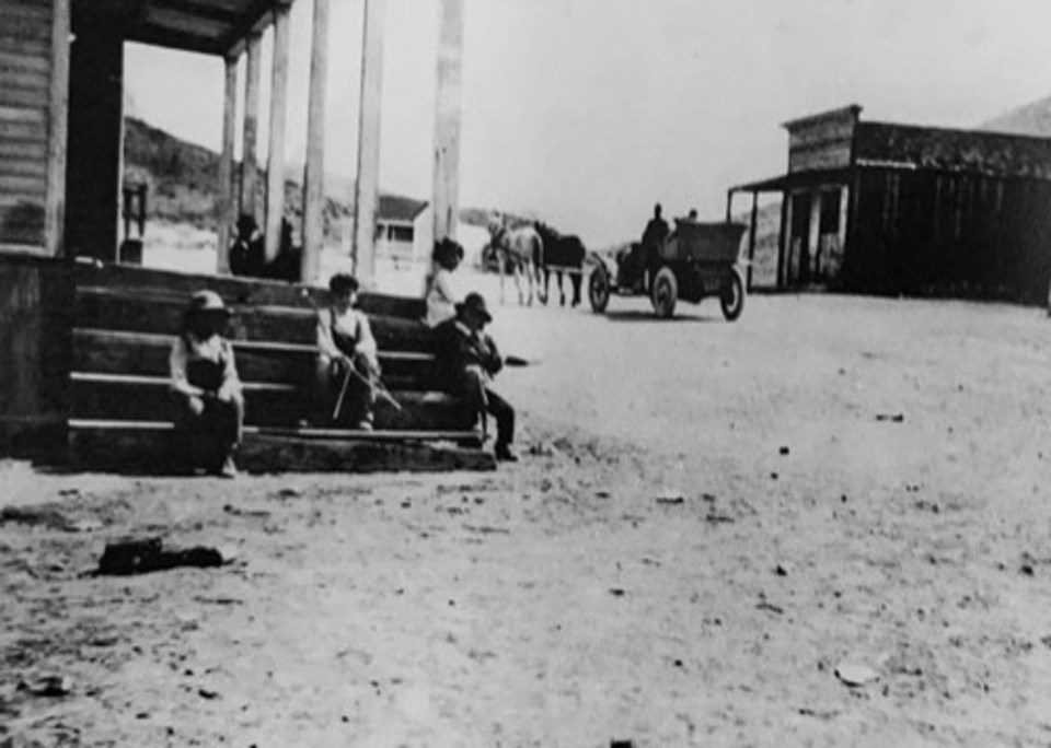 Boys sitting on steps with old car driving by.