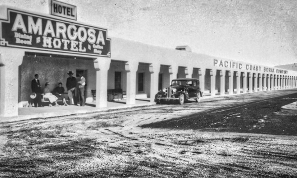 Men in front of old stucco building with car in front.