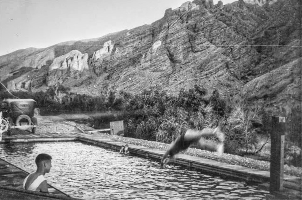 Young men in swimming pool with rocky canyon in background.