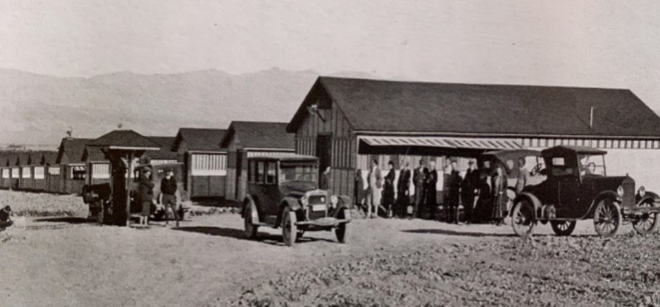 People standing next to buildings with old cars in front.