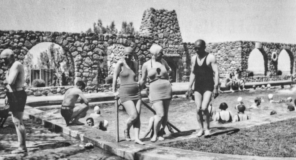 People in bathing suits standing and swimming around pool.