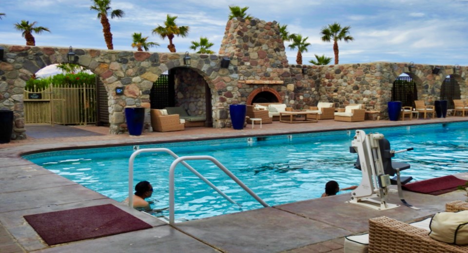 People in bathing suits standing and swimming around pool.