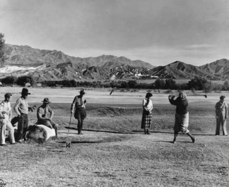 Men and women play golf with desert mountains in background