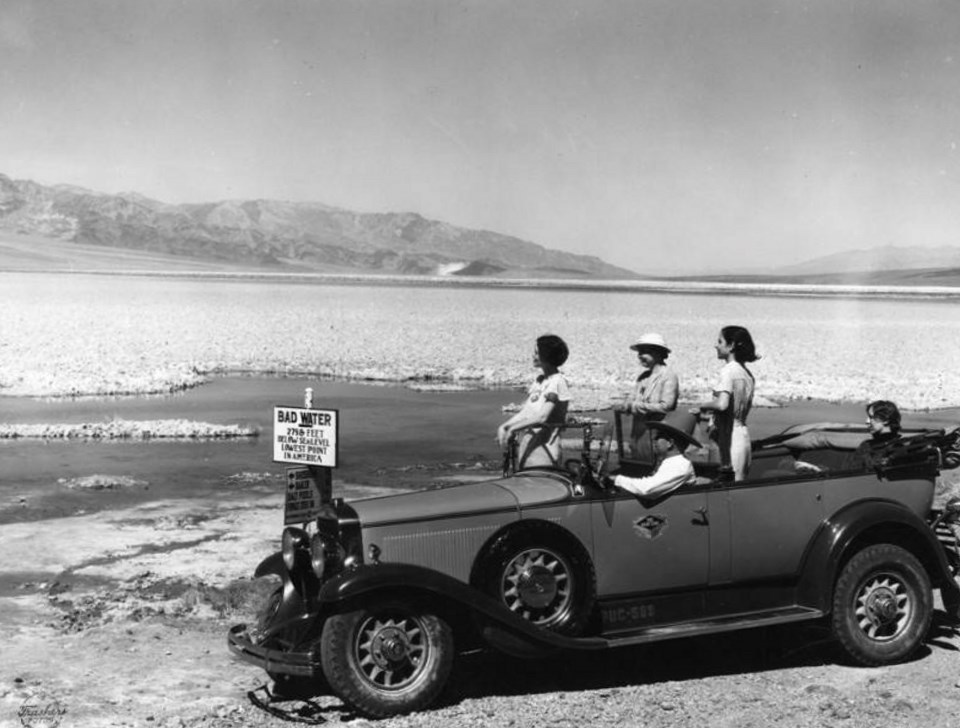 People in a car standing and looking at water in desert.