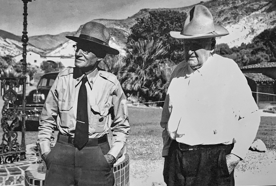 Two men in front of a fountain with hills in background.