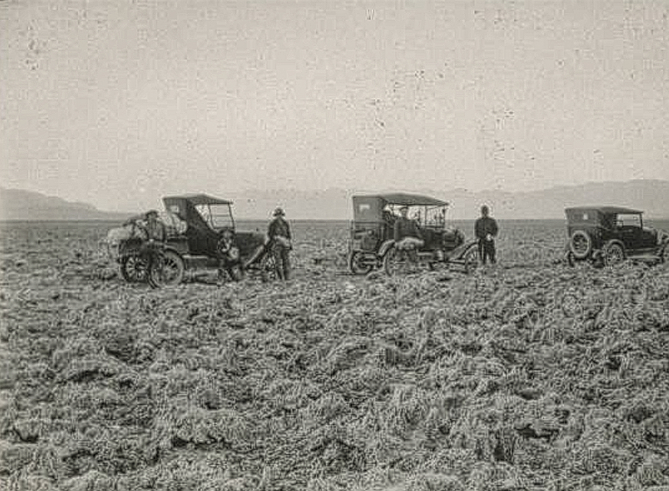 Men and three old cars crossing very rocky landscape.