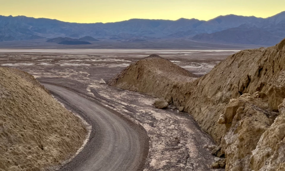 An old car drives on dirt road into dried mud canyon.