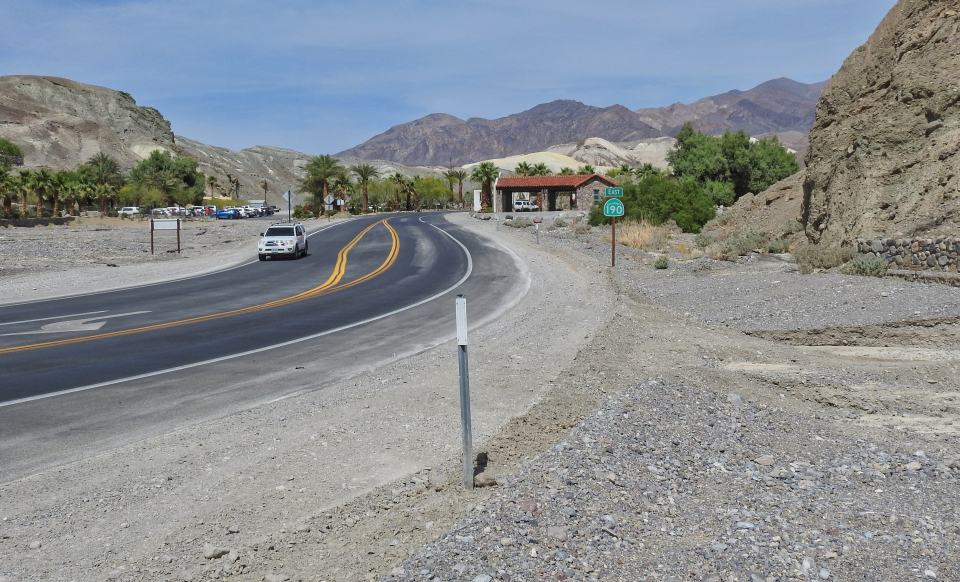 Rushing water covers road with buildings and mountains in background.