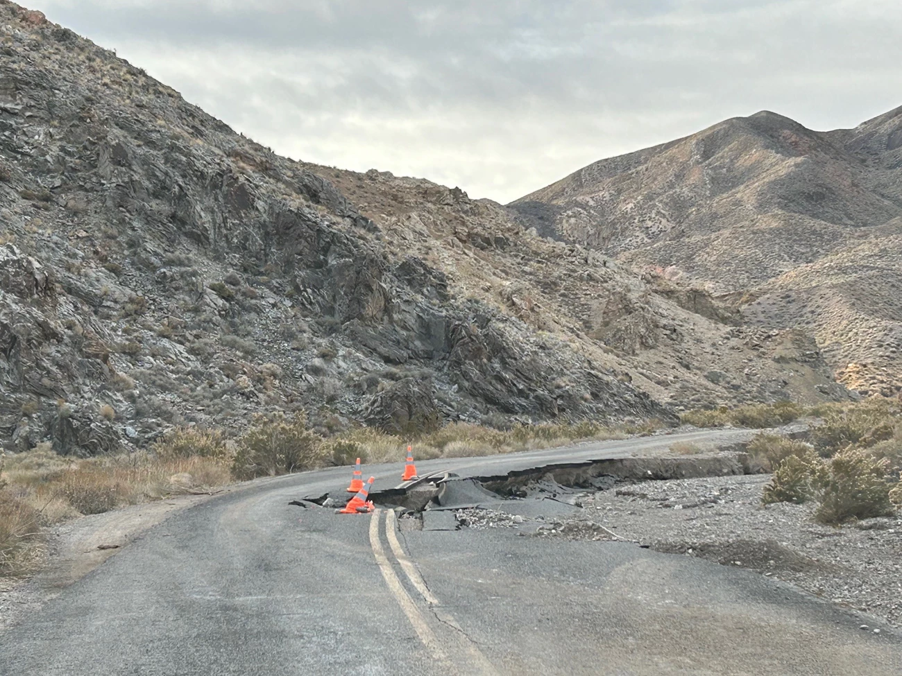 Orange cones mark a collapsed section of road.