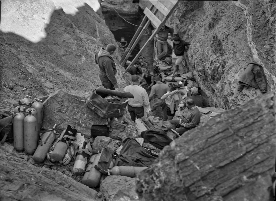 A group of people with SCUBA diving equipment in rocky pool.