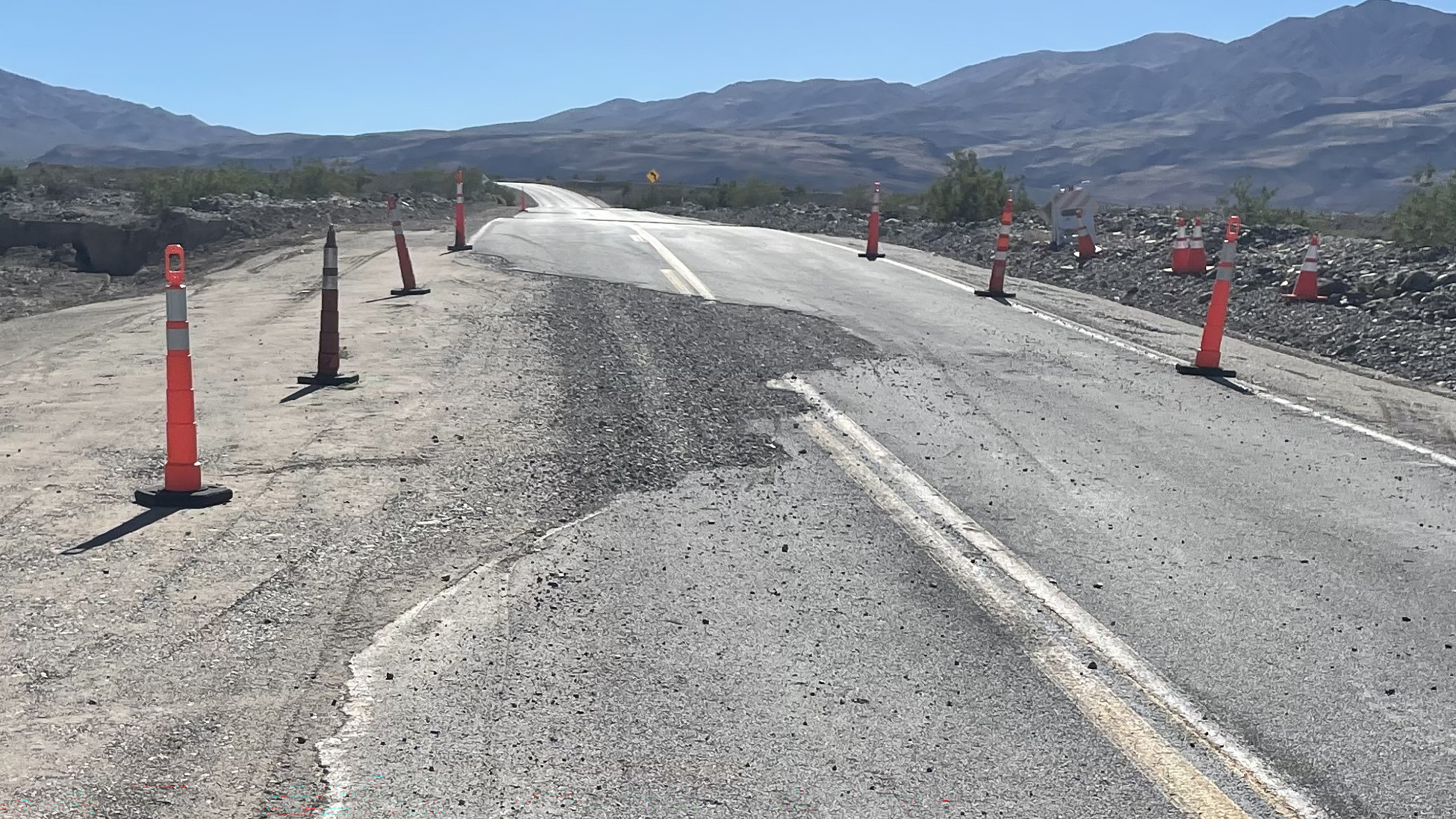 Broken pavement along a road leading into a desert mountain landscape.
