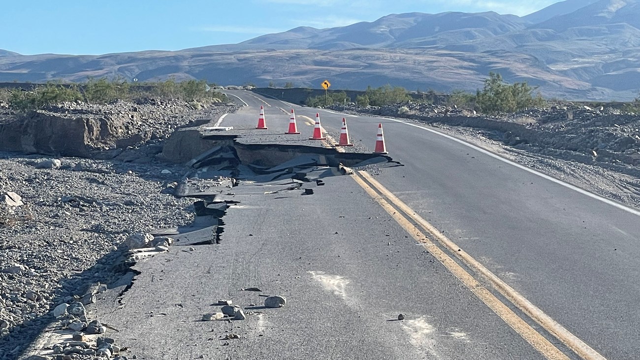 Broken pavement along a road leading into a desert mountain landscape.